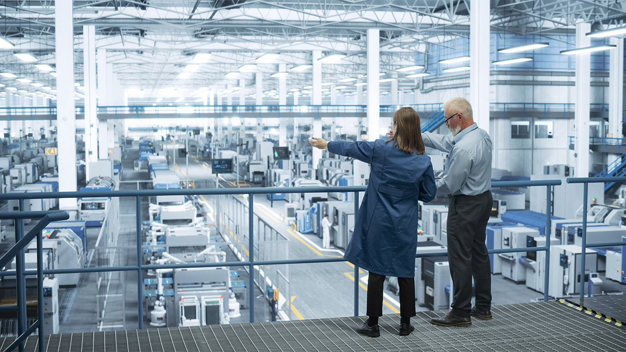 Two people on a gantry, looking across a manufacturing facility