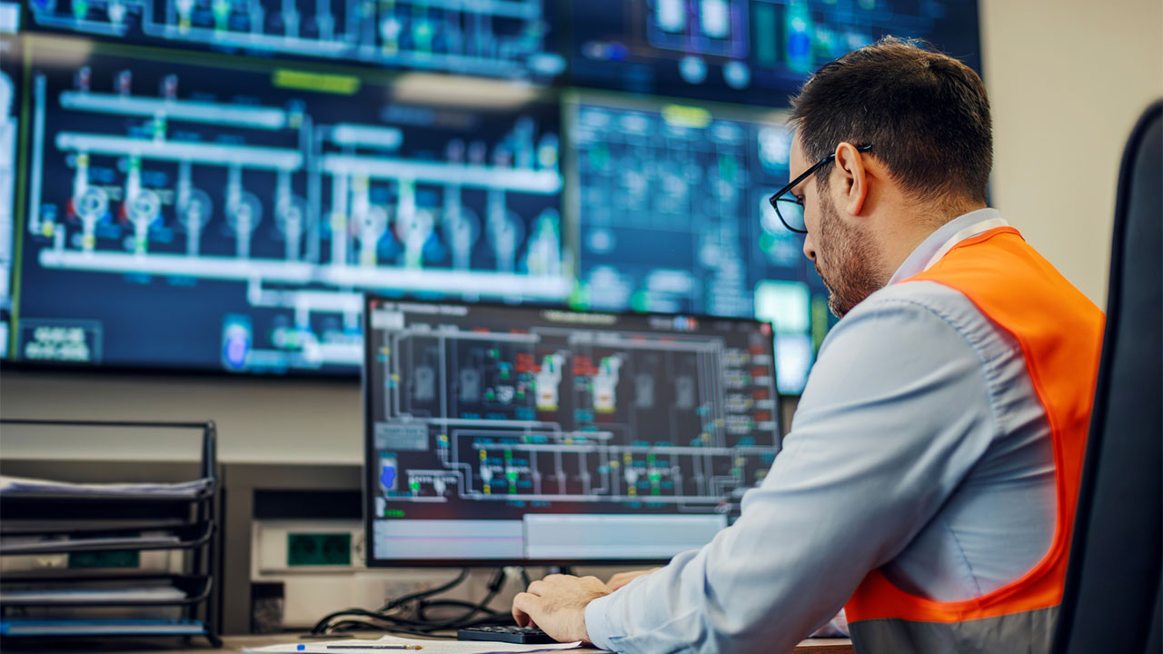 An engineer monitoring multiple computer screens displaying complex industrial diagrams