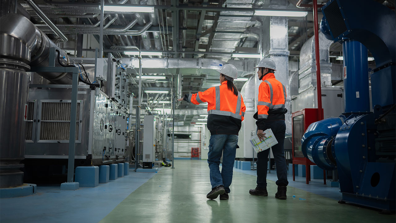 Two engineers in high visibility jackets inspect an industrial facility