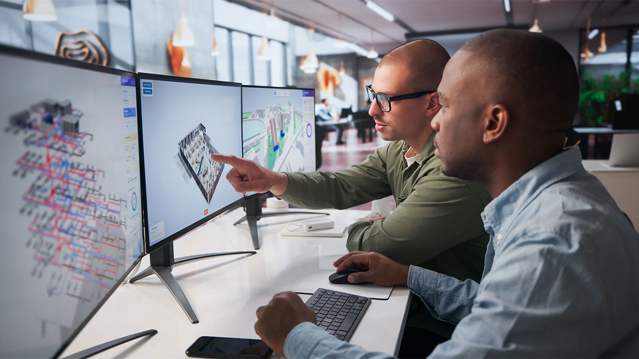 Two people looking at a set of computer monitors