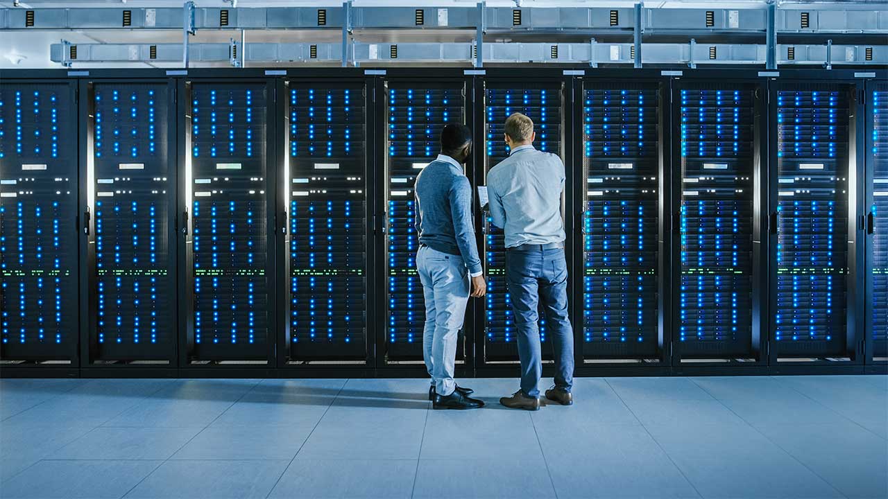Two people standing in front of a rack of servers, examining and discussing their setup