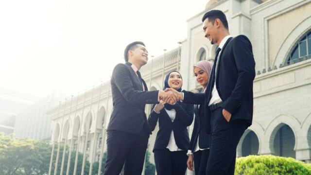 Group of people in suits shaking hands and smiling outside a building